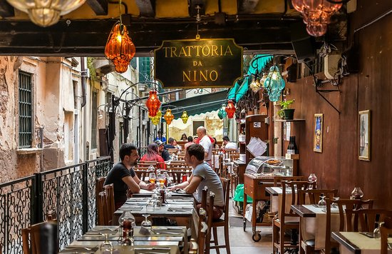Outdoor seating at a traditional Venice trattoria along a narrow canal
