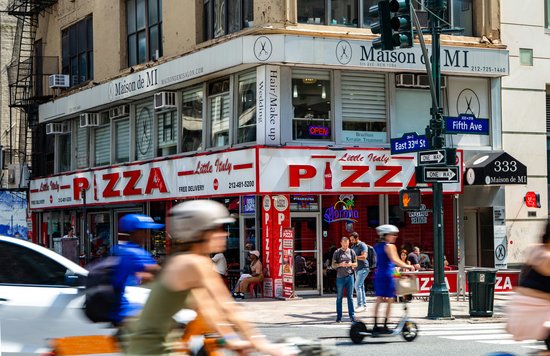 A busy street corner with a pizza restaurant in New York City