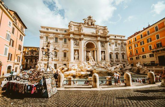 A large fountain structure with detailed sculptures surrounded by colored buildings