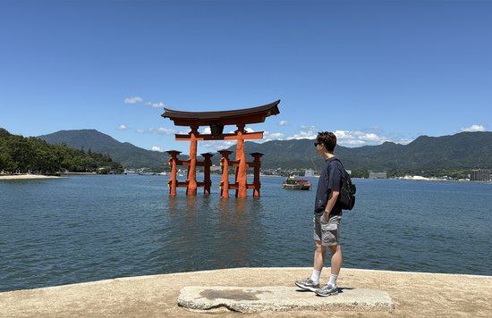 Man taking a photo in front of the floating torii gates in Itsukushima Shrine