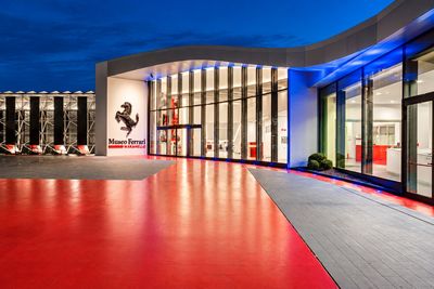 Exterior view of the Ferrari Museum in Maranello, Italy, featuring its modern glass entrance, iconic Ferrari logo and illuminated architecture.