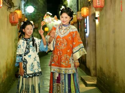 暖黄灯笼映亮古巷,橙红绣袍女子与青花衣少女共持鱼灯,笑意盈盈,尽显徽州夜巷里的烟火温情与民俗意趣