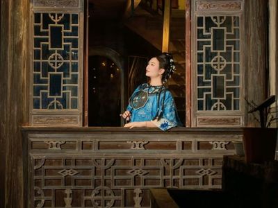 蓝底绣纹清式华服女子,倚于雕花木窗,轻执团扇,侧望凝思,古窗棂与暖光交织,尽显徽派古宅的雅致意境