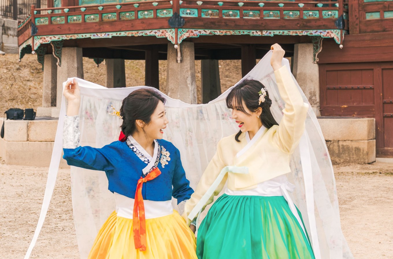 Two ladies wearing traditional hanboks while happily smiling at each other
