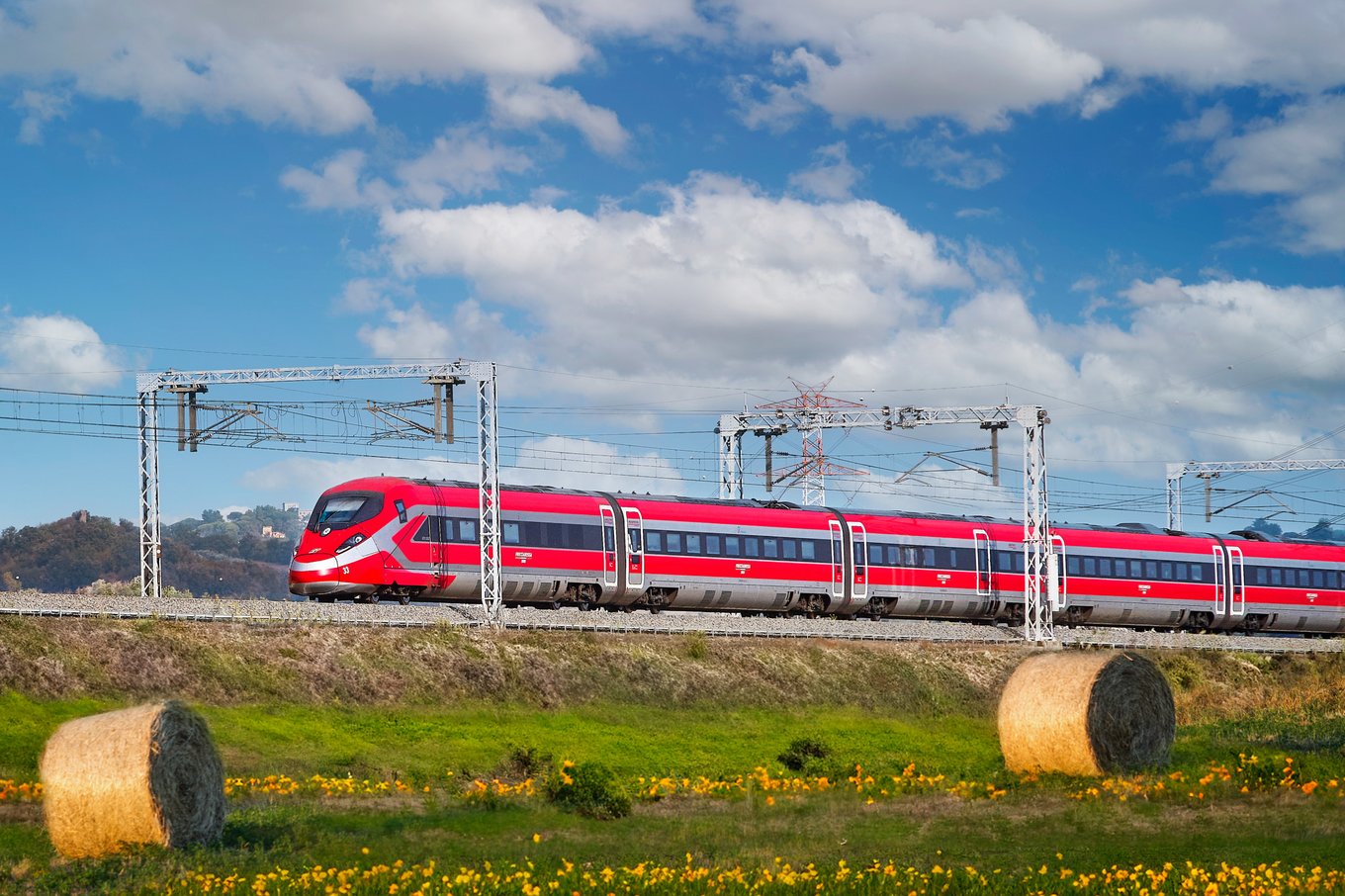 Red Trenitalia Frecciarossa train passing by fields and hills in Italy