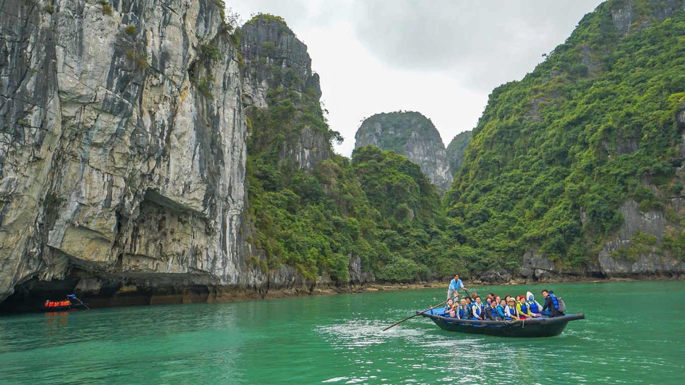 Tourists on a bamboo boat surrounded by towering limestone cliffs in Halong Bay