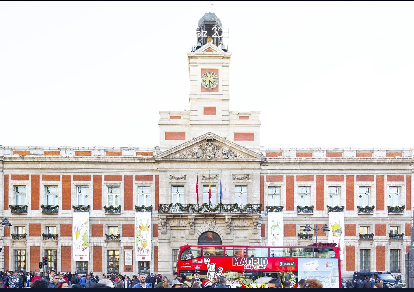Red sightseeing bus in front of Puerta del Sol building in Madrid
