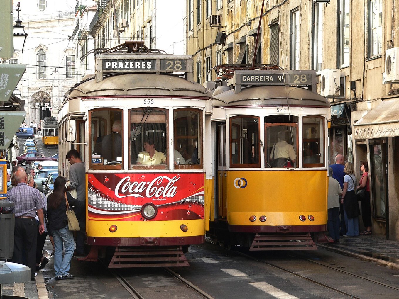Two Tram 28 trams traveling through a narrow, crowded Lisbon street