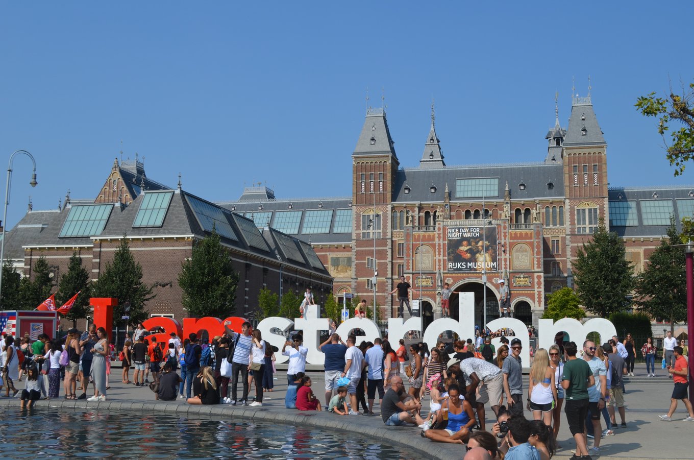 Tourists gathered around the I Amsterdam sign in Museumplein with the Rijksmuseum behind