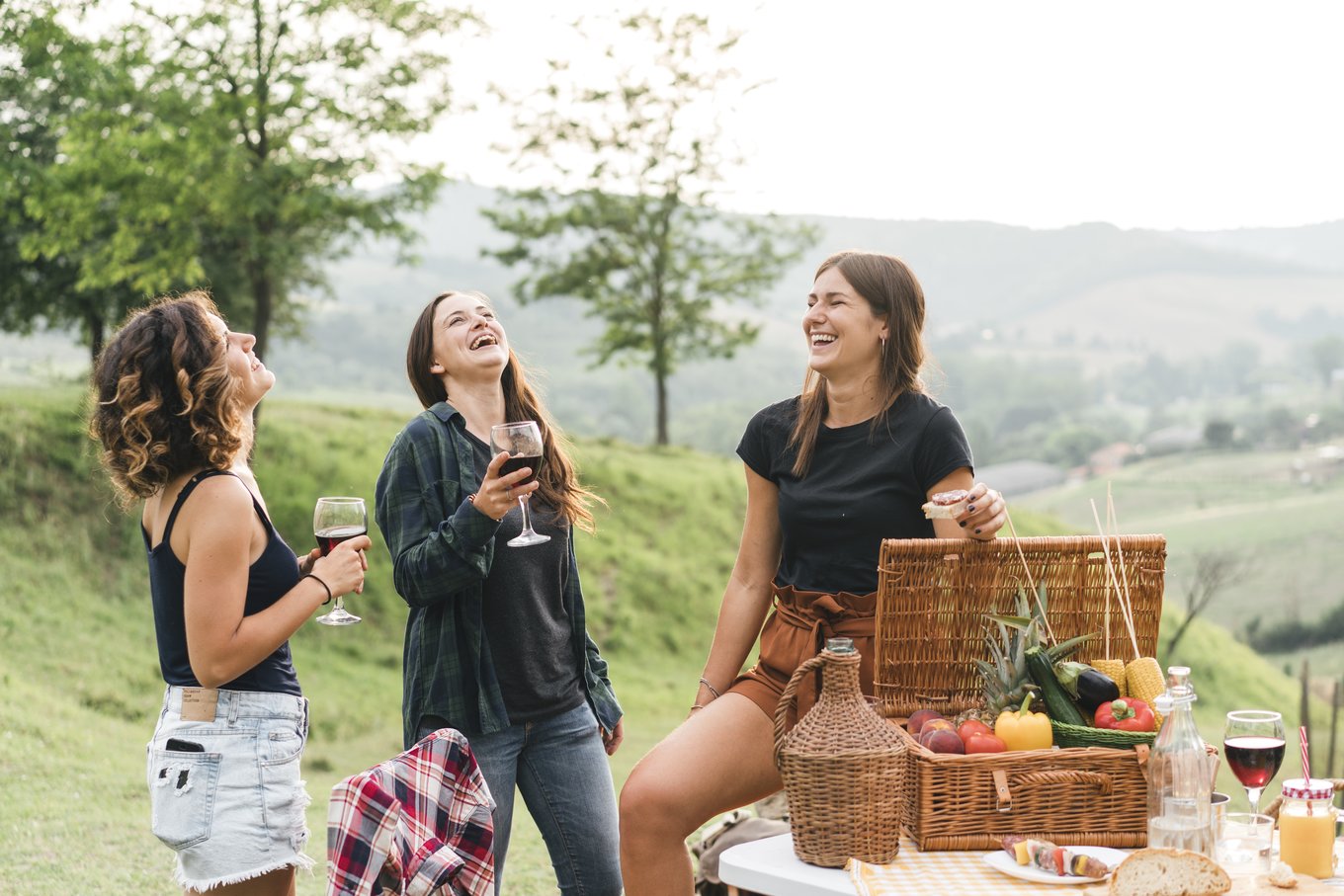 Friends enjoying a budget-friendly group trip picnic, sharing laughs, food, and wine outdoors together