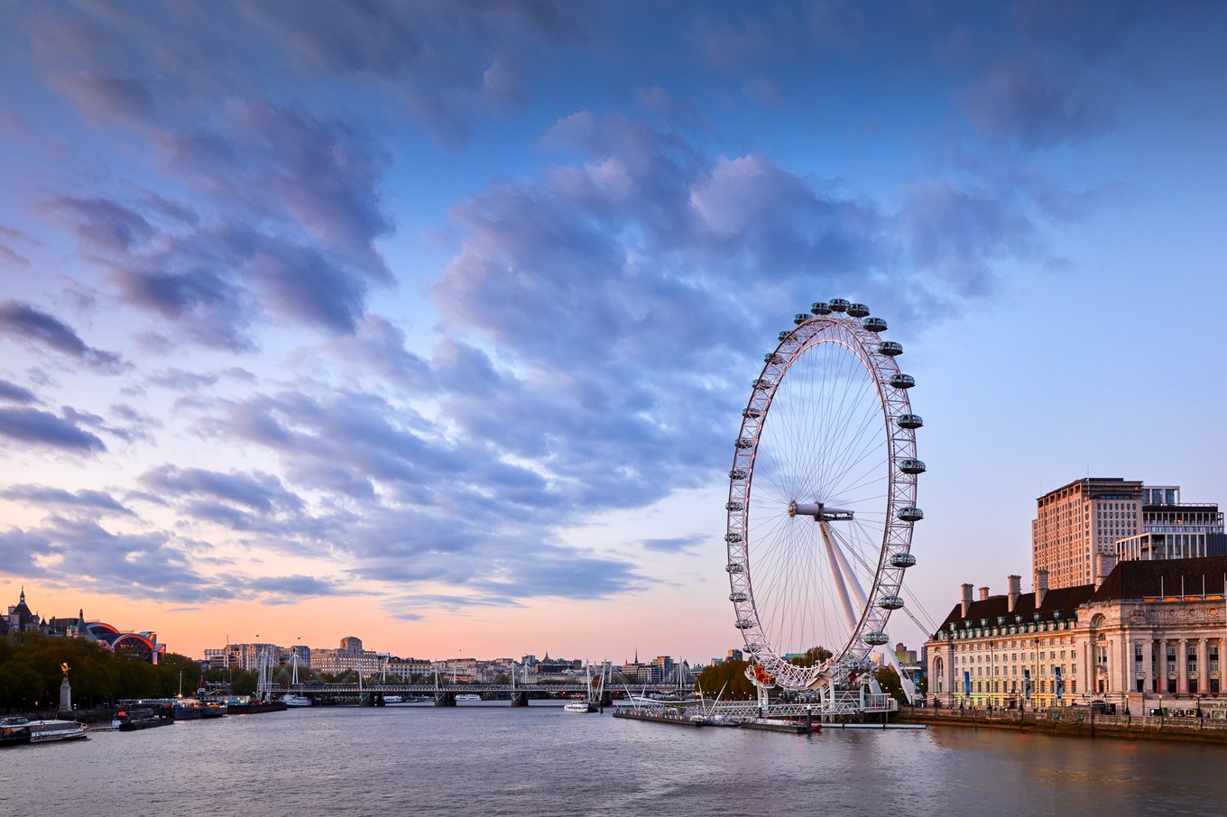 A ferris wheel and buildings against a sunset from the perspective of someone riding a boat on a river