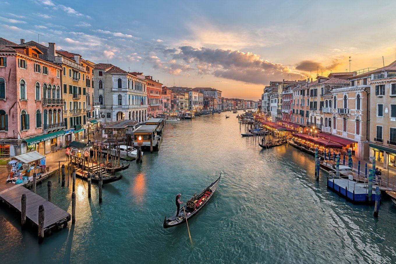 Gondola cruising the Grand Canal at sunset with glowing city lights