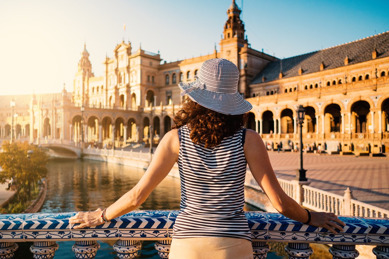 Traveler overlooking historic Spanish plaza with canal and arches at sunset