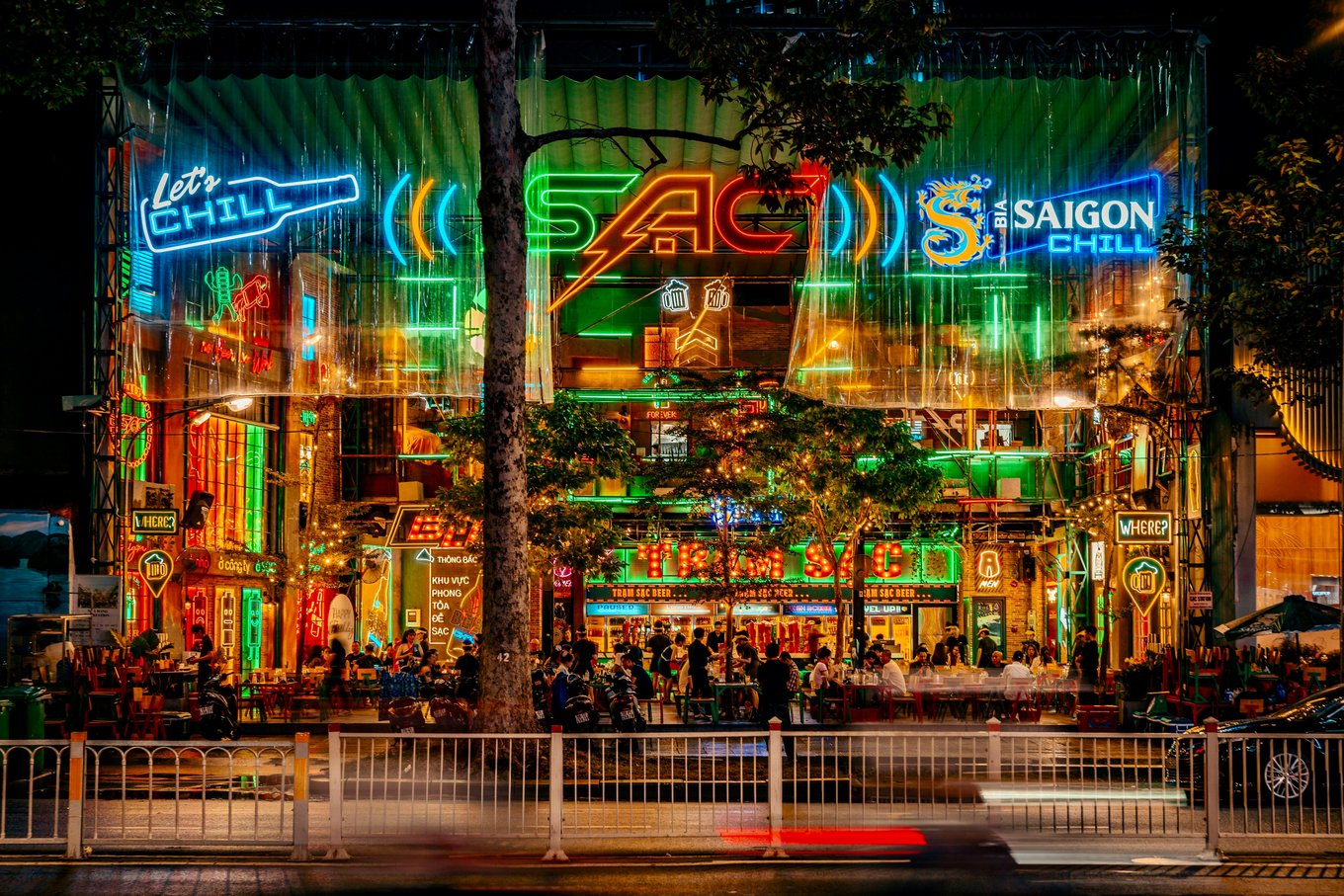 Busy nightlife street in Ho Chi Minh City with neon bar signs and crowds enjoying drinks at night