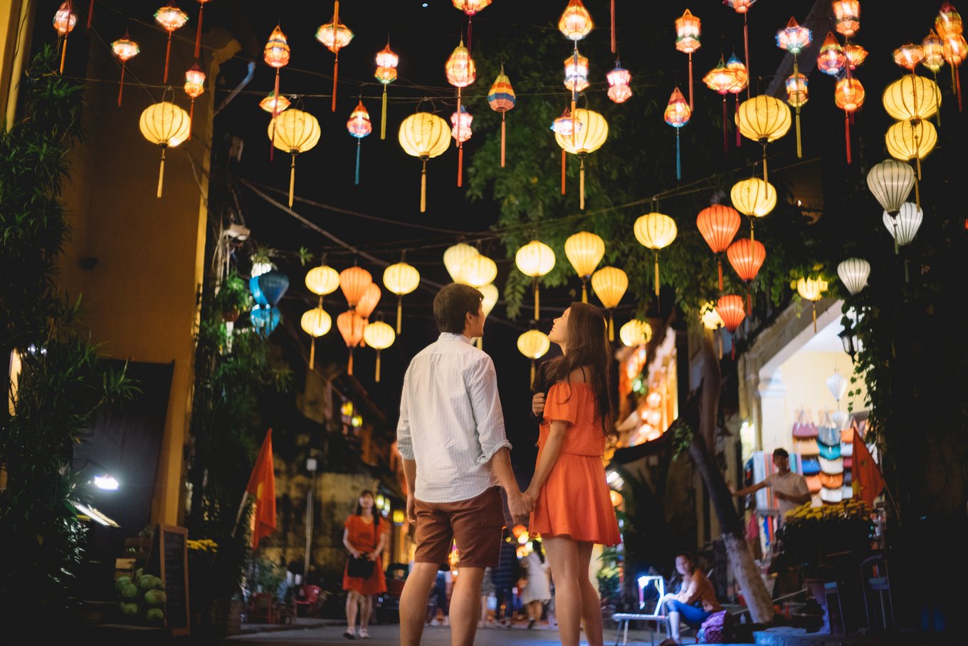 Couple walking hand in hand under colourful lanterns in Hoi An at night.
