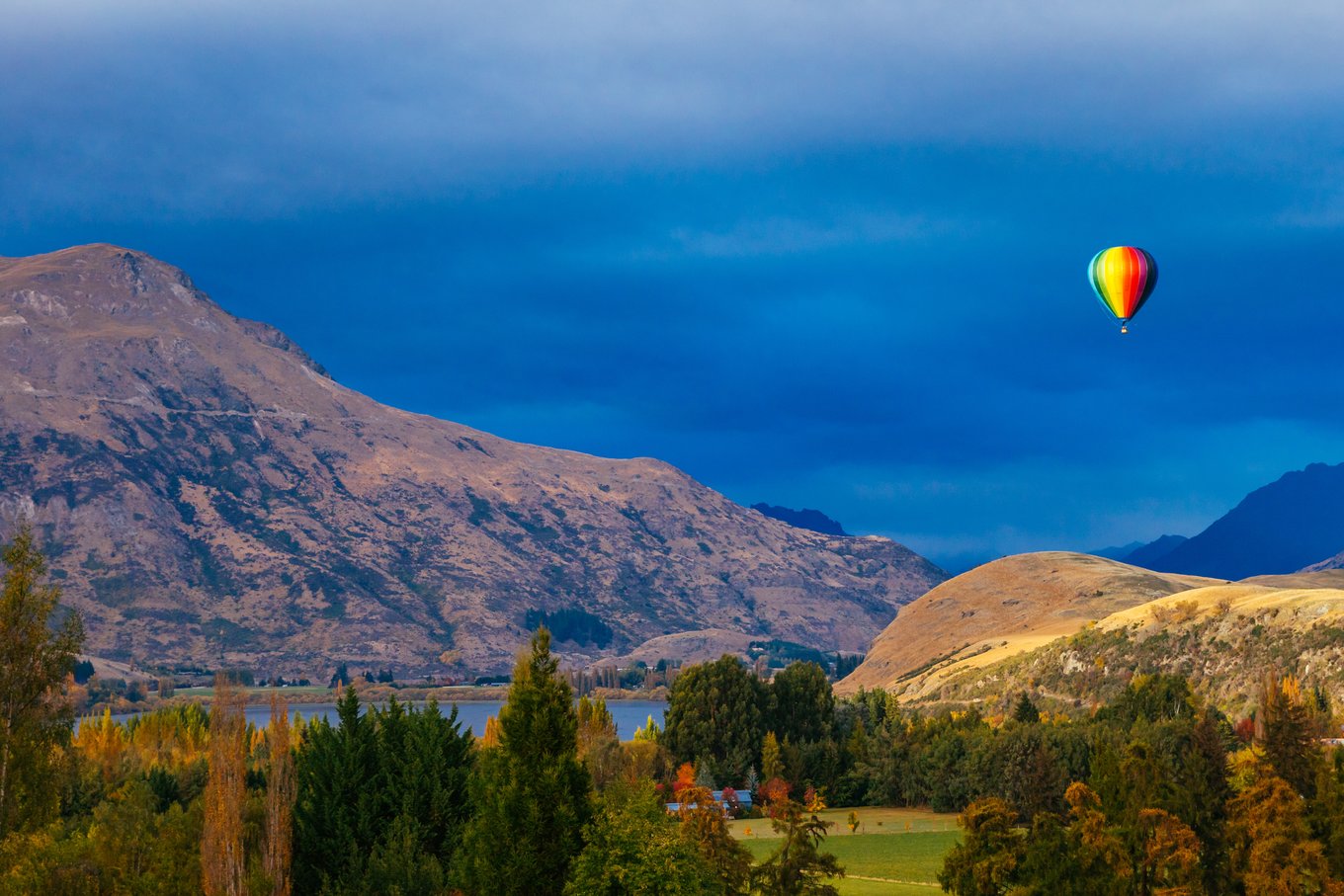 Rainbow hot air balloon above golden autumn trees and mountains in Queenstown