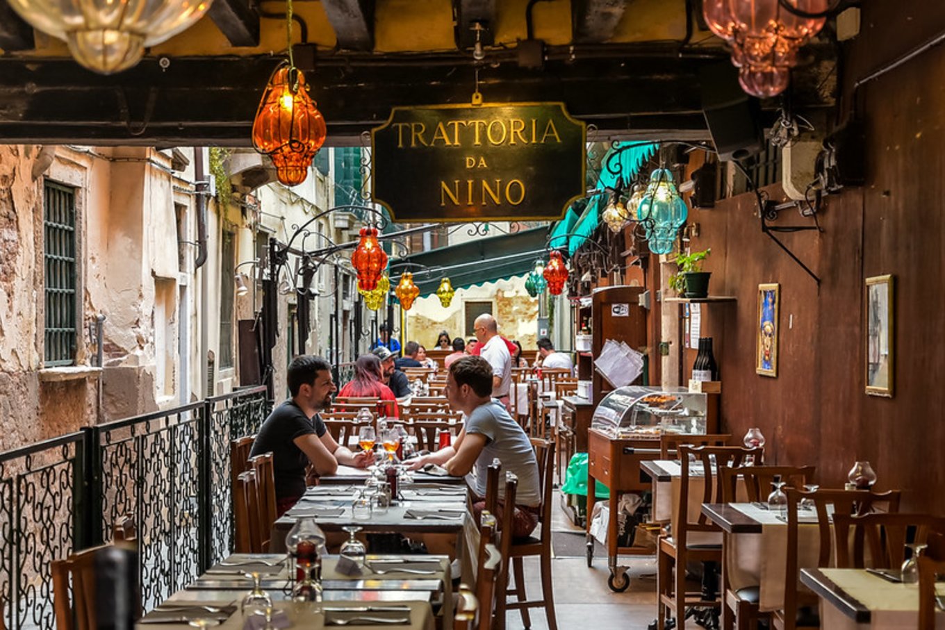 Outdoor seating at a traditional Venice trattoria along a narrow canal
