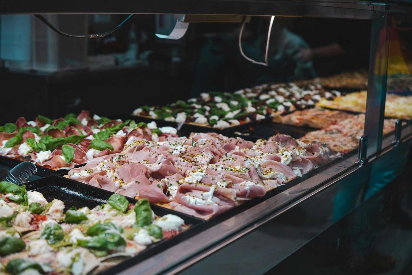 Roman-style pizza slices with different toppings like prosciutto, cheese, and herbs | Photo Credit: gaspifilms on Unsplash