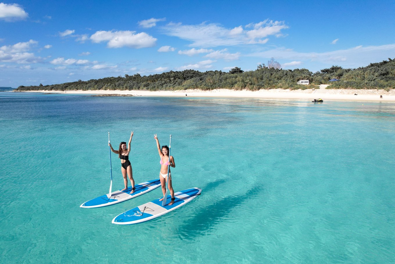 Travelers paddleboarding in clear blue water at a beach in Okinawa