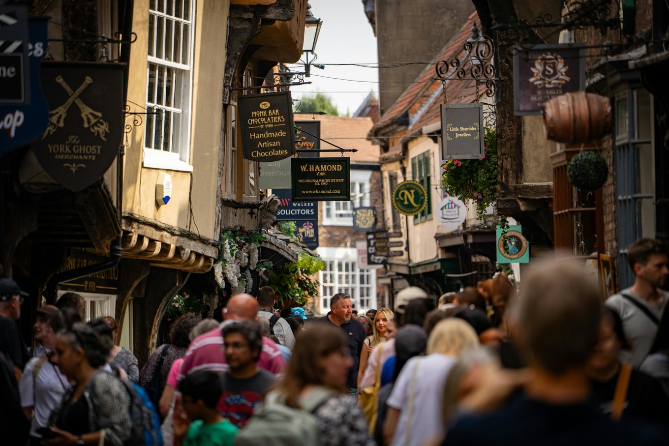 Crowded street in York with shops, hanging signs, and people walking through a narrow lane