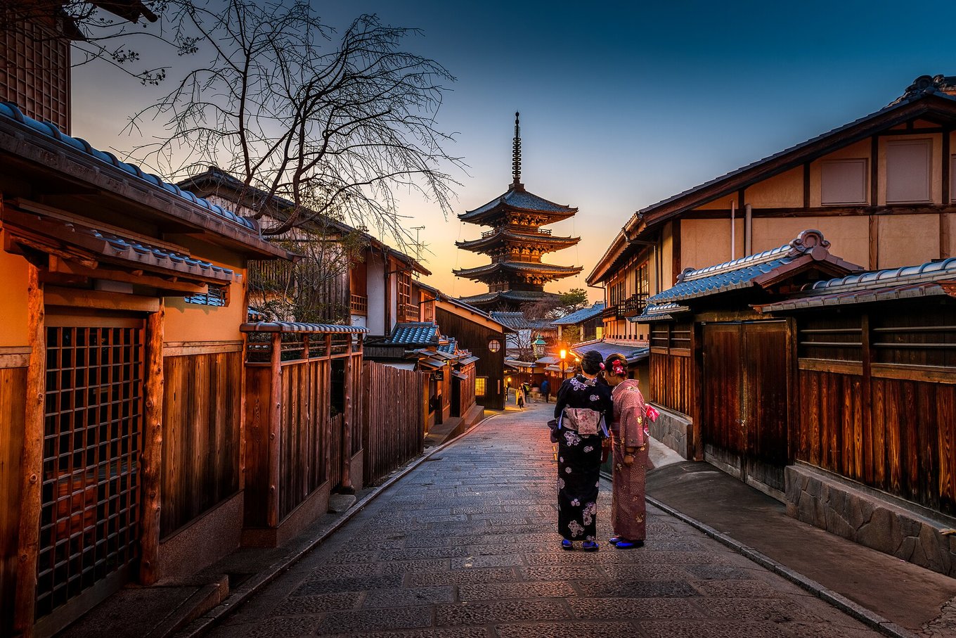 Two women wearing a kimono stand in the middle of a street where the Hokanji-Temple can be seen