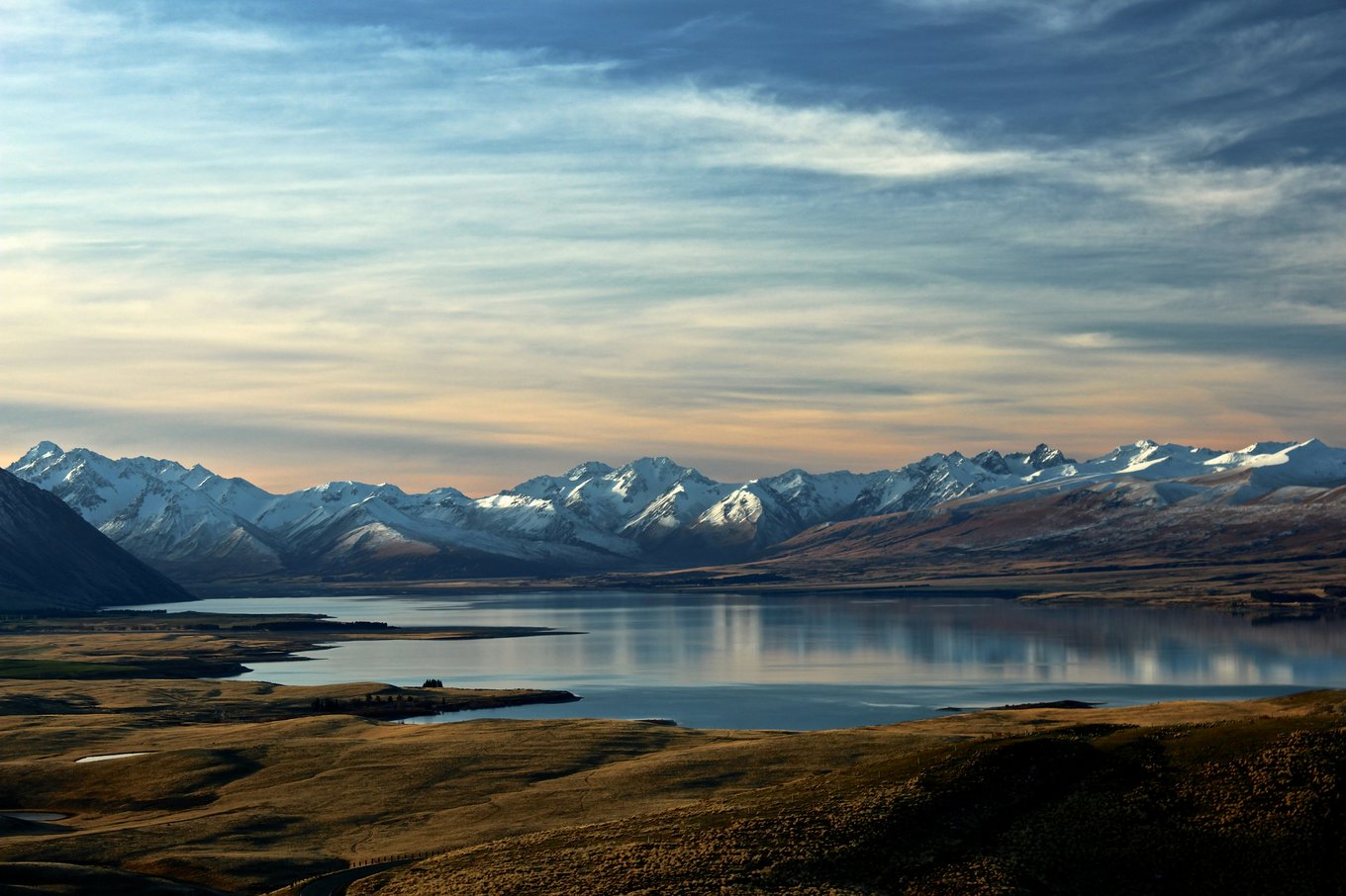 A snow-capped mountainscape behind a lake at dusk.