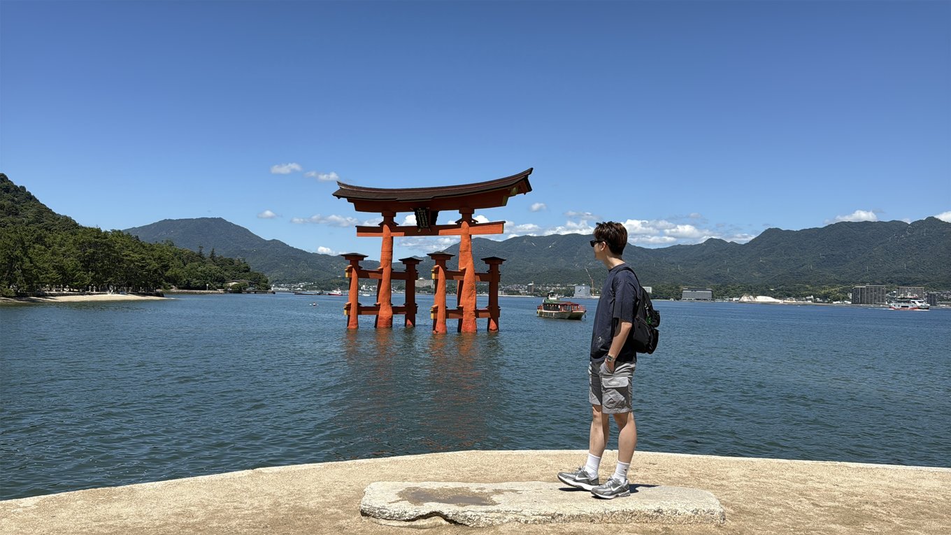 Man taking a photo in front of the floating torii gates in Itsukushima Shrine