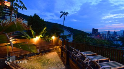 An open-air hot spring terrace in Beitou at dusk, city lights below