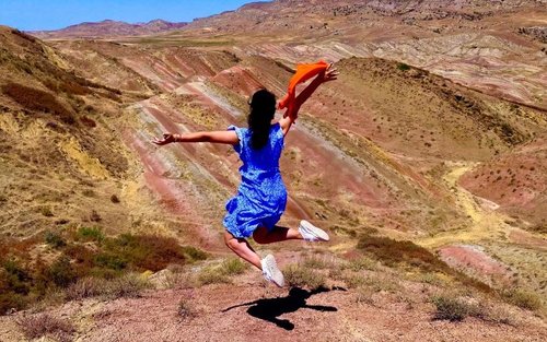 A woman jumping in front of Rainbow Mountains
