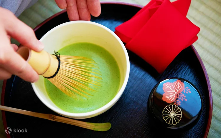 Matcha being whisked in a tea bowl, with a lacquered sweets container beside it