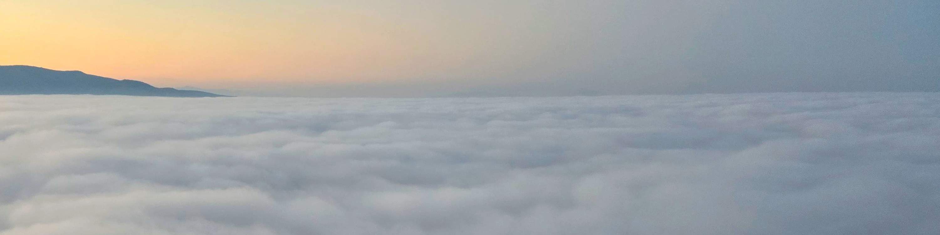 Über nebelverhangene Wolken gleiten, während der leuchtende Sonnenaufgang den Horizont in warmen Farbtönen malt