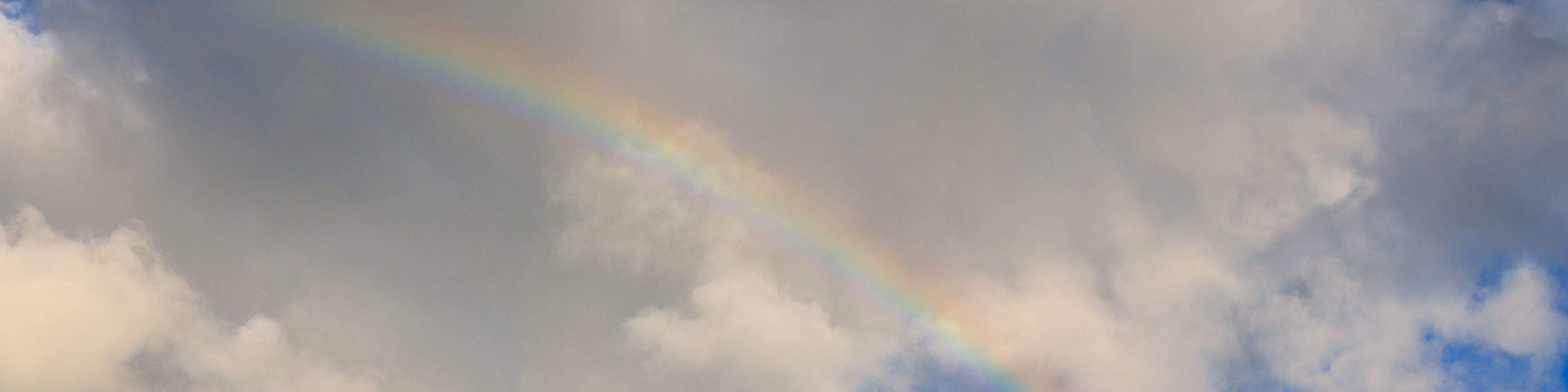 Un vibrante arcoíris se extiende por el cielo con el barco navegando debajo.