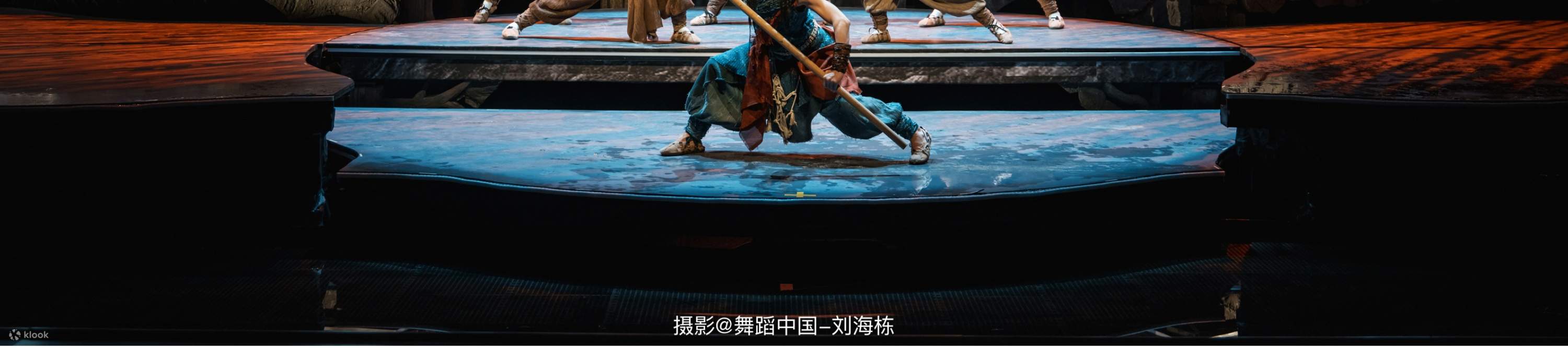 On a multi-layered stage, unified costumes, coordinated with ropes and props, and a realistic mountain rock background create a scene where their movements are orderly and full of power, as if they are performing a collective labor of an ancient tribe.