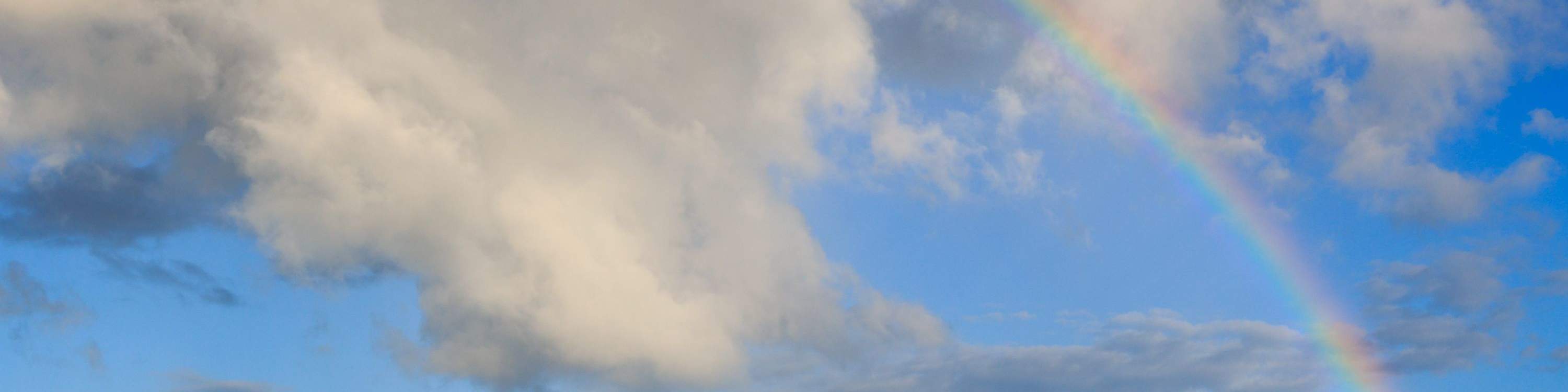 Un vibrante arcoíris se extiende por el cielo con el barco navegando debajo.