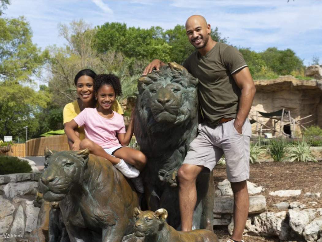 Một gia đình tươi cười rạng rỡ, tạo dáng chụp ảnh bên cạnh tượng sư tử biểu tượng tại San Antonio Zoo