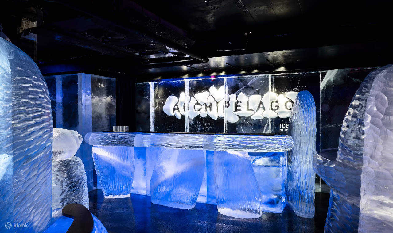 Des tabourets et des tables en glace cristalline scintillent sous des lumières bleues dans un décor de bar glacé.