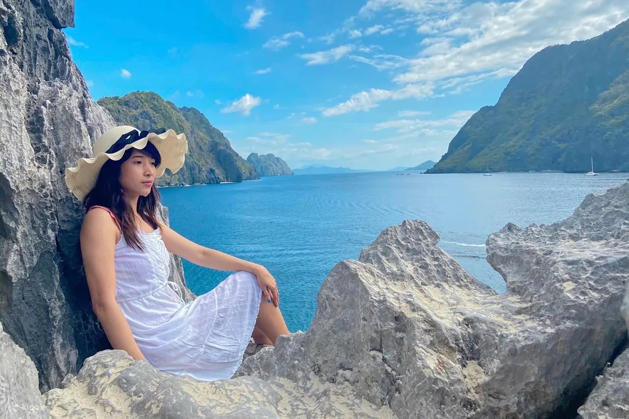 戴着宽边帽的女人坐在岩石上，背景是爱妮岛的风景