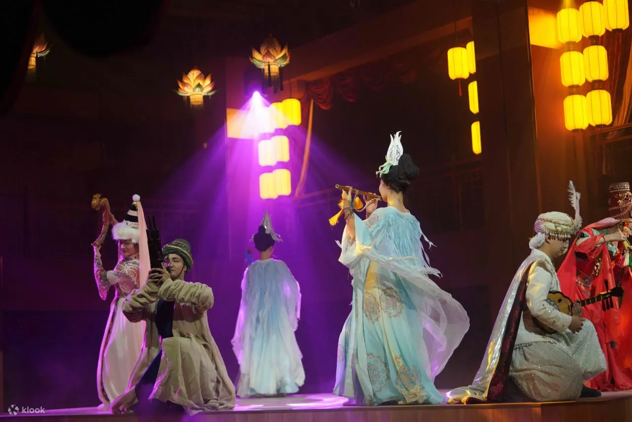 舞台上演员们服饰各异，尽显丝路沿线多元风情。有的吹奏乐器，有的弹奏弦乐，在暖黄与紫调灯光交织下，营造出神秘而绮丽的氛围，仿佛奏响丝路千年的悠扬旋律，传递着文化交融的独特韵味