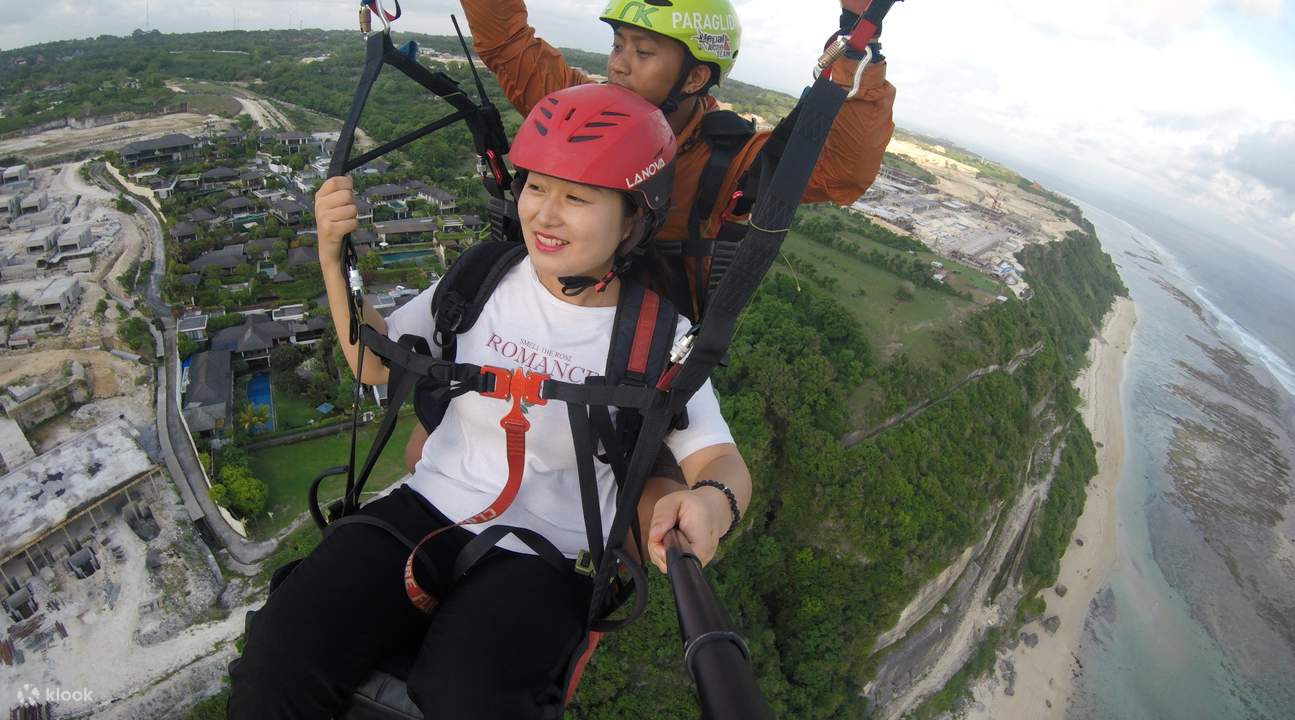 seorang wanita dan lelaki membentuk hati dengan tangan mereka semasa melakukan aktiviti paragliding