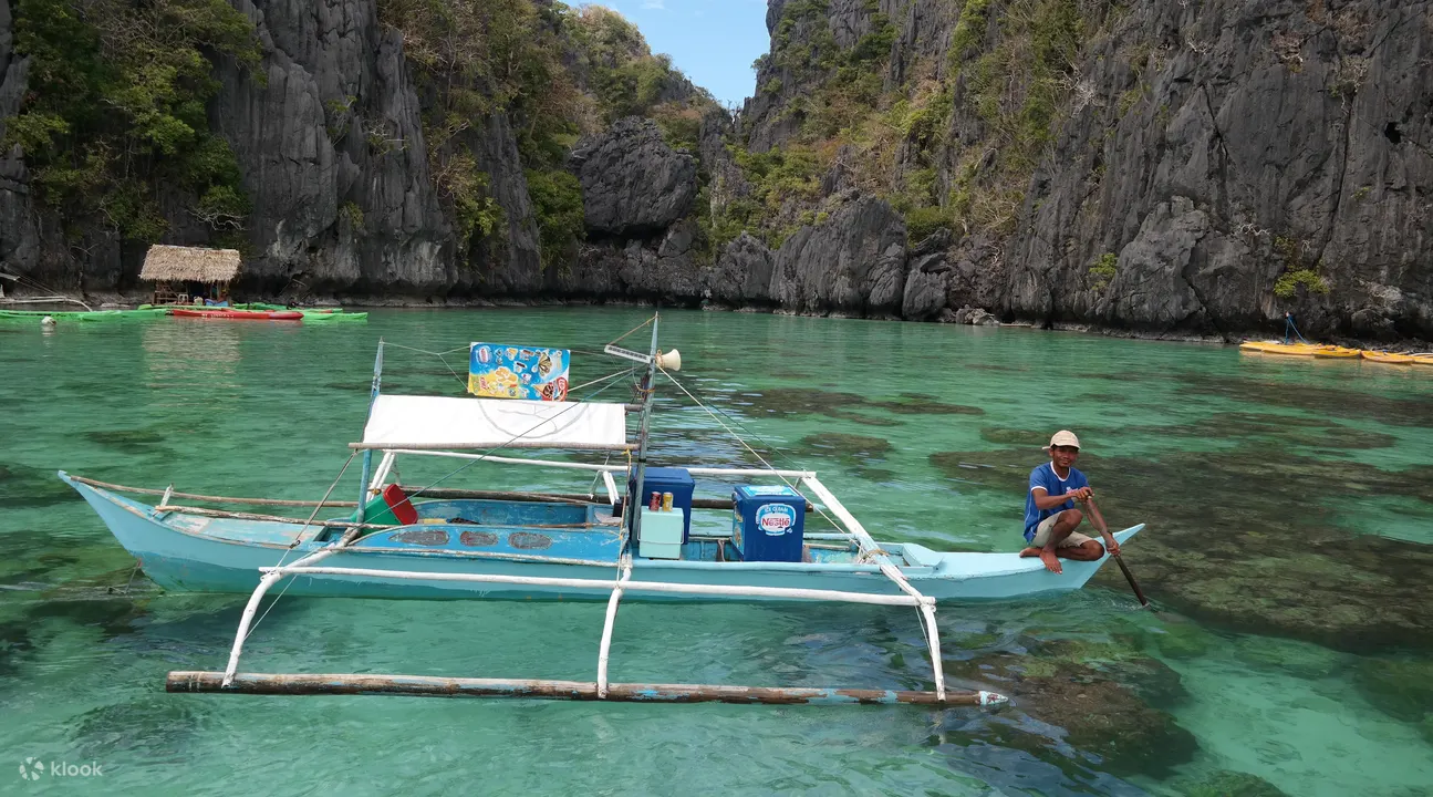 blue-green colored boat on the water with a person sitting on the right edge of the boat