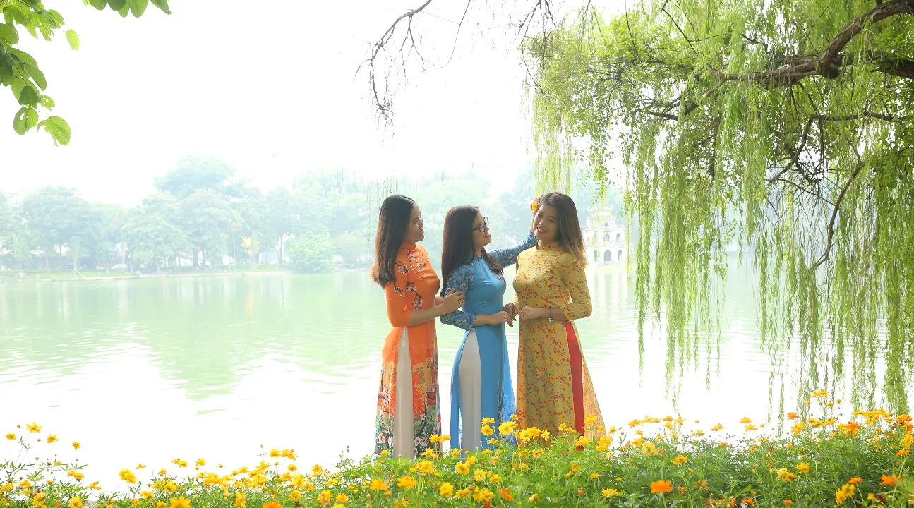 women wearing ao dais posing by a lake