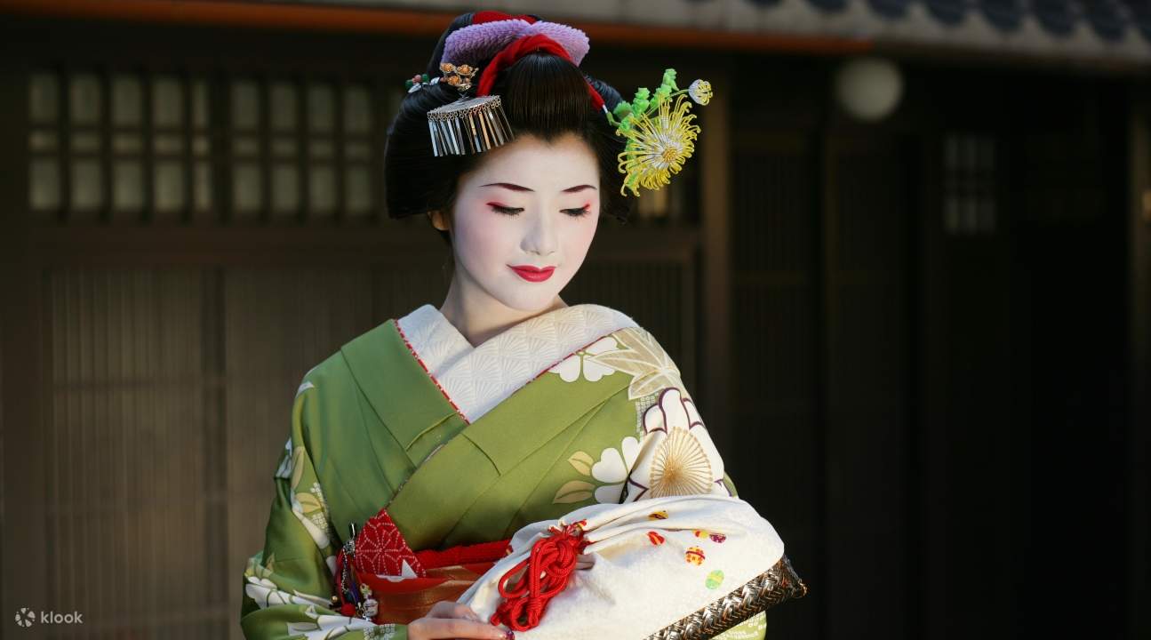 a maiko in a light green kimono carrying a purse