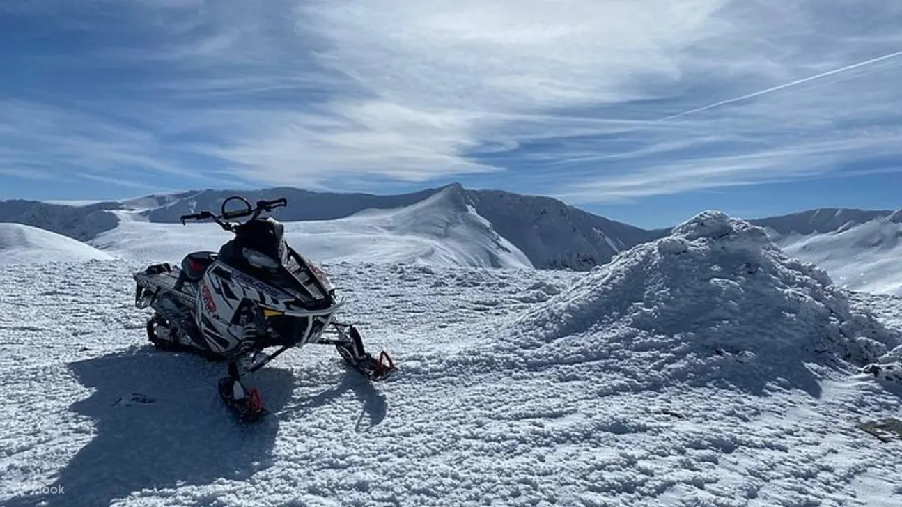 一辆雪地摩托车骄傲地停在路边，背景是雄伟的山峰