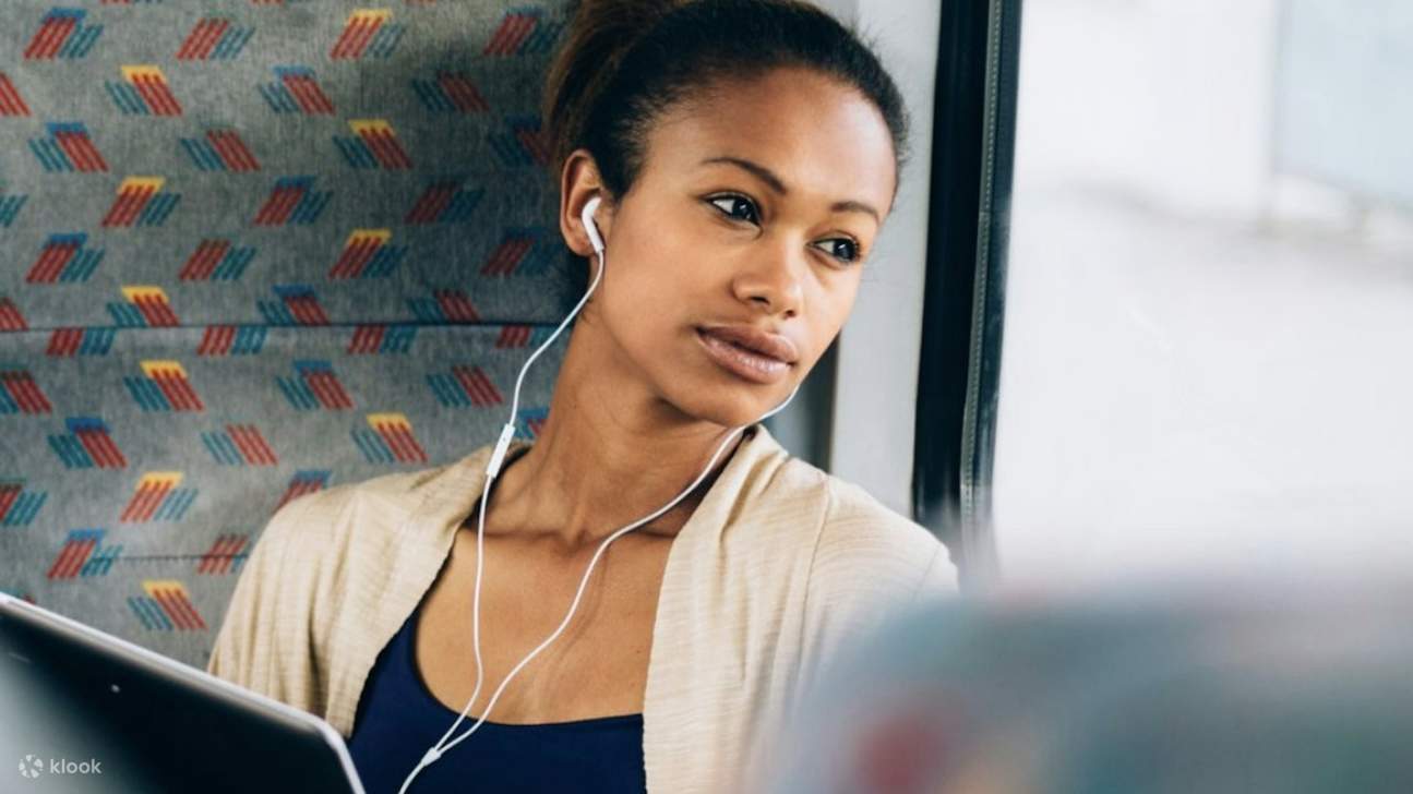 Seorang wanita santai tersenyum, duduk dengan nyaman di dalam kursi bus yang luas dan bersih
