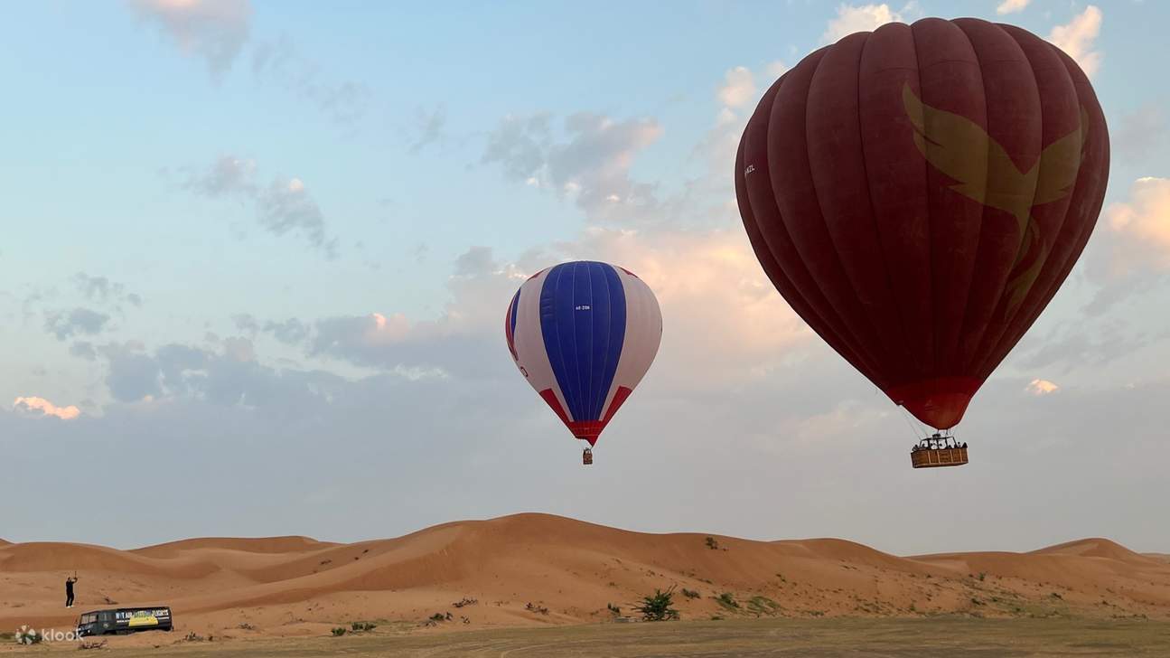 Balon udara panas melayang anggun di atas gurun keemasan, menawarkan pemandangan panorama yang menakjubkan
