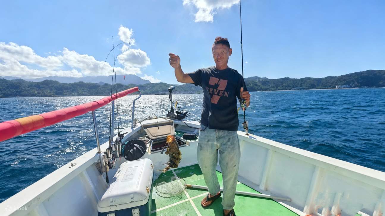 钓友在蓝色的渔船上，手持一条体型硕大的海鱼，身后是嶙峋的礁石。每一次抛竿都可能收获惊喜，体验与大鱼博弈的刺激。