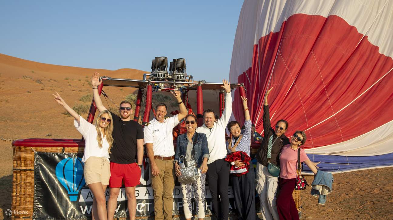 Sekelompok orang yang gembira merayakan petualangan balon udara mereka yang tak terlupakan di padang pasir