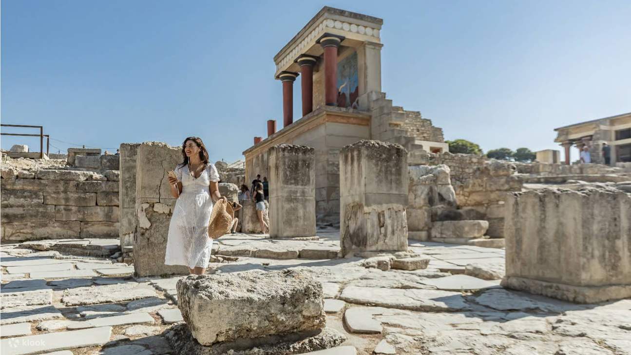 Un visitante caminando entre las antiguas ruinas del Palacio de Knossos bajo el cielo azul despejado