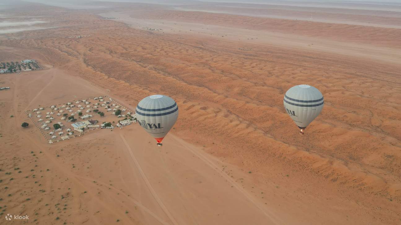 드넓은 사막의 모래 언덕 위로 여러 개의 열기구가 하늘을 향해 떠오르는 아름다운 광경을 감상하세요.