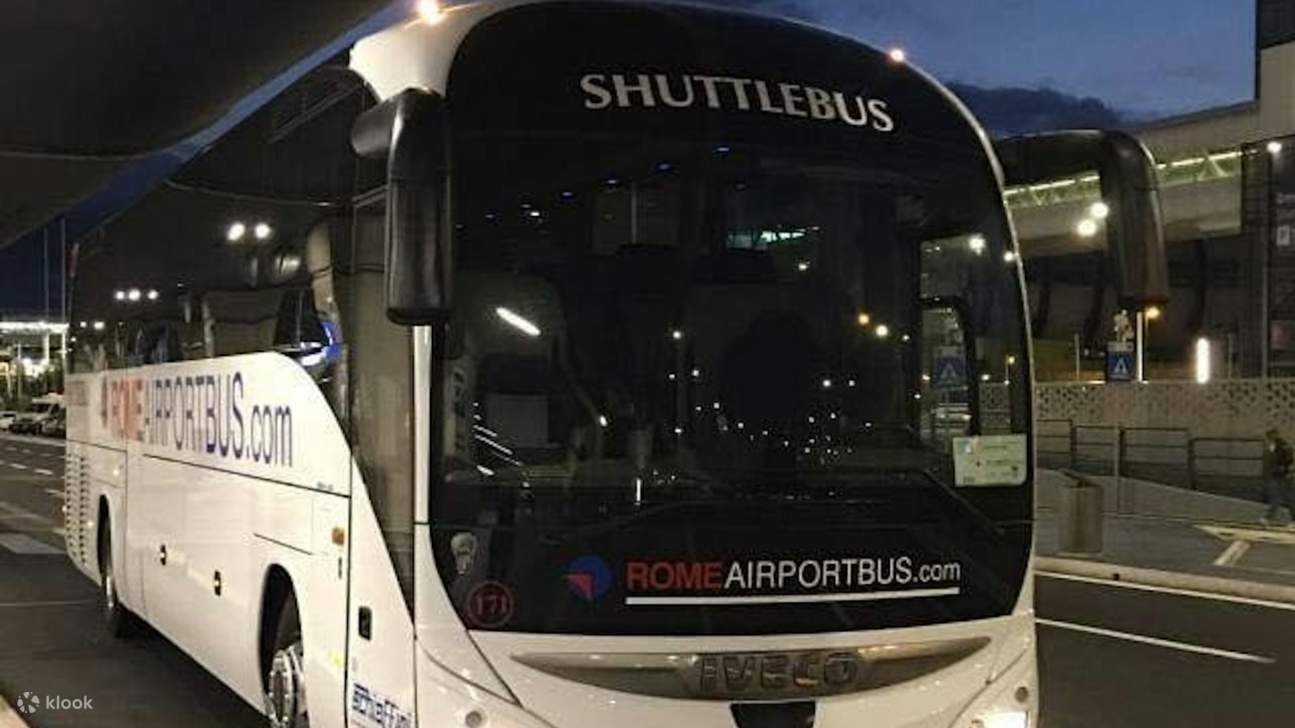 Bus transportasi putih ramping dengan papan nama Roma, diparkir di tepi terminal bandara